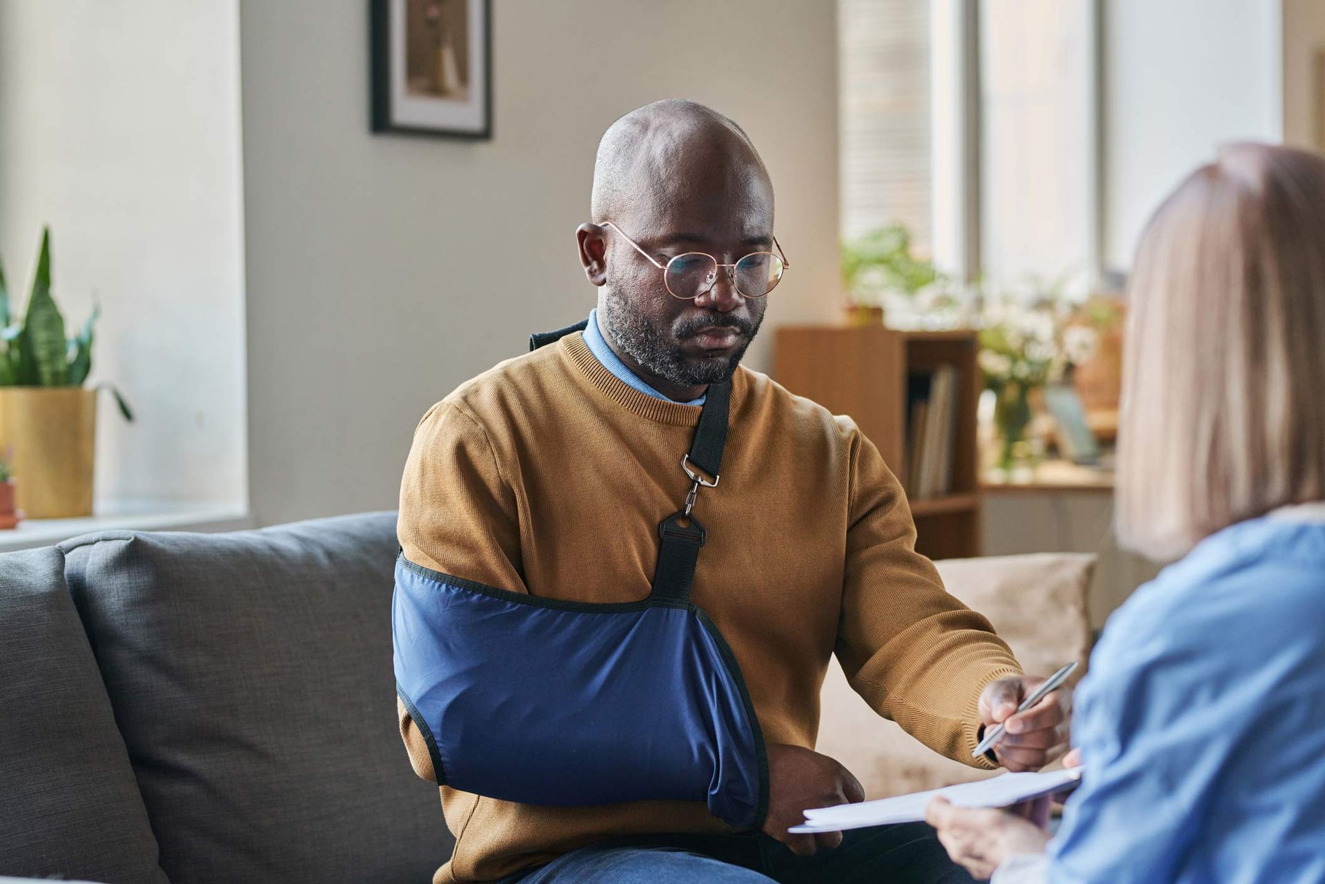 Man with arm sling signs paperwork while meeting with a person. Man with arm sling signs paperwork while meeting with a person.
