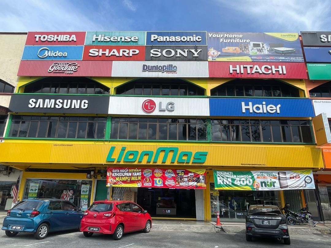 Yellow and white electronics store with various brand signs. Cars parked in front.