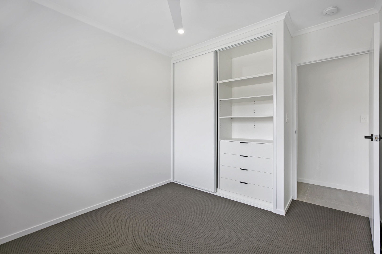 Empty white bedroom with built-in closet, shelves, and drawers. Grey carpet. Open doorway on right. — Morrison Cabinetry in Cedar Pocket, QLD