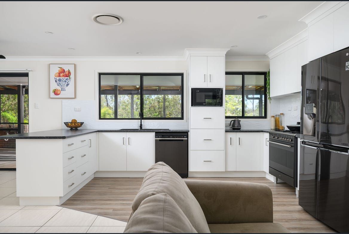 Modern kitchen with white cabinets, black appliances, and a dark-framed window overlooking greenery — Morrison Cabinetry in Sunshine Coast, QLD