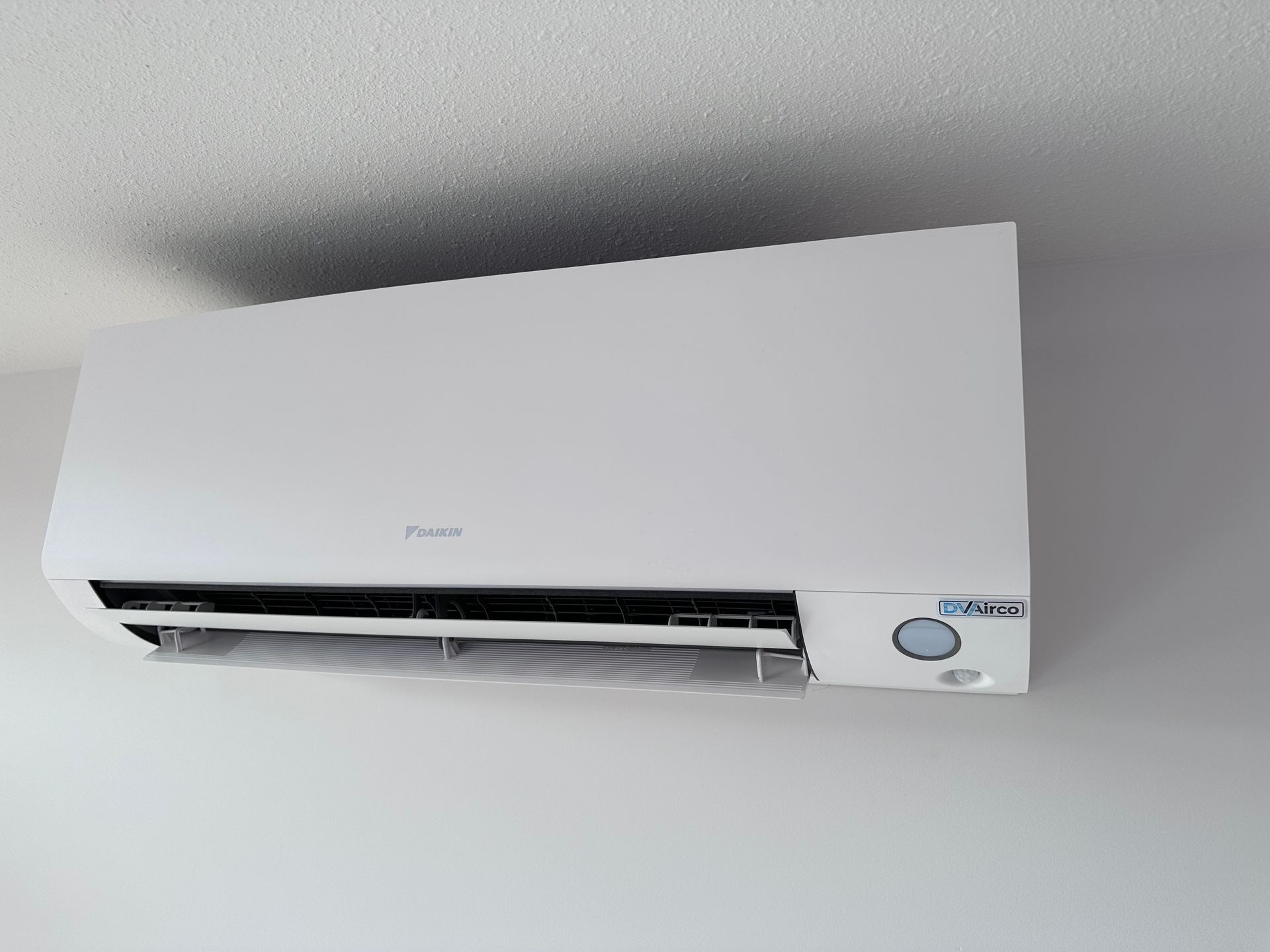 Een witte airconditioner hangt aan het plafond in een kamer.