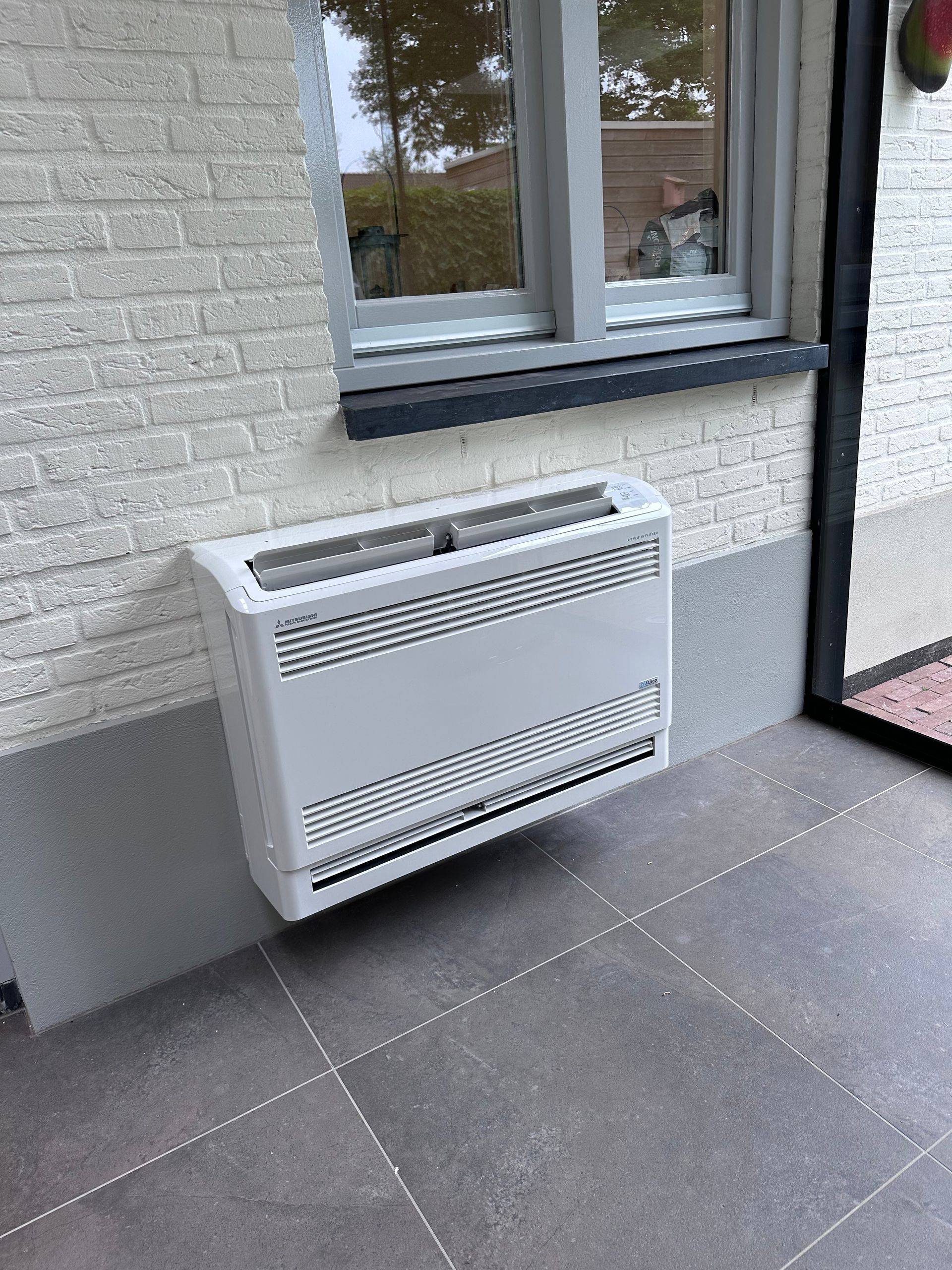 Een witte airconditioner hangt aan een witte muur.
