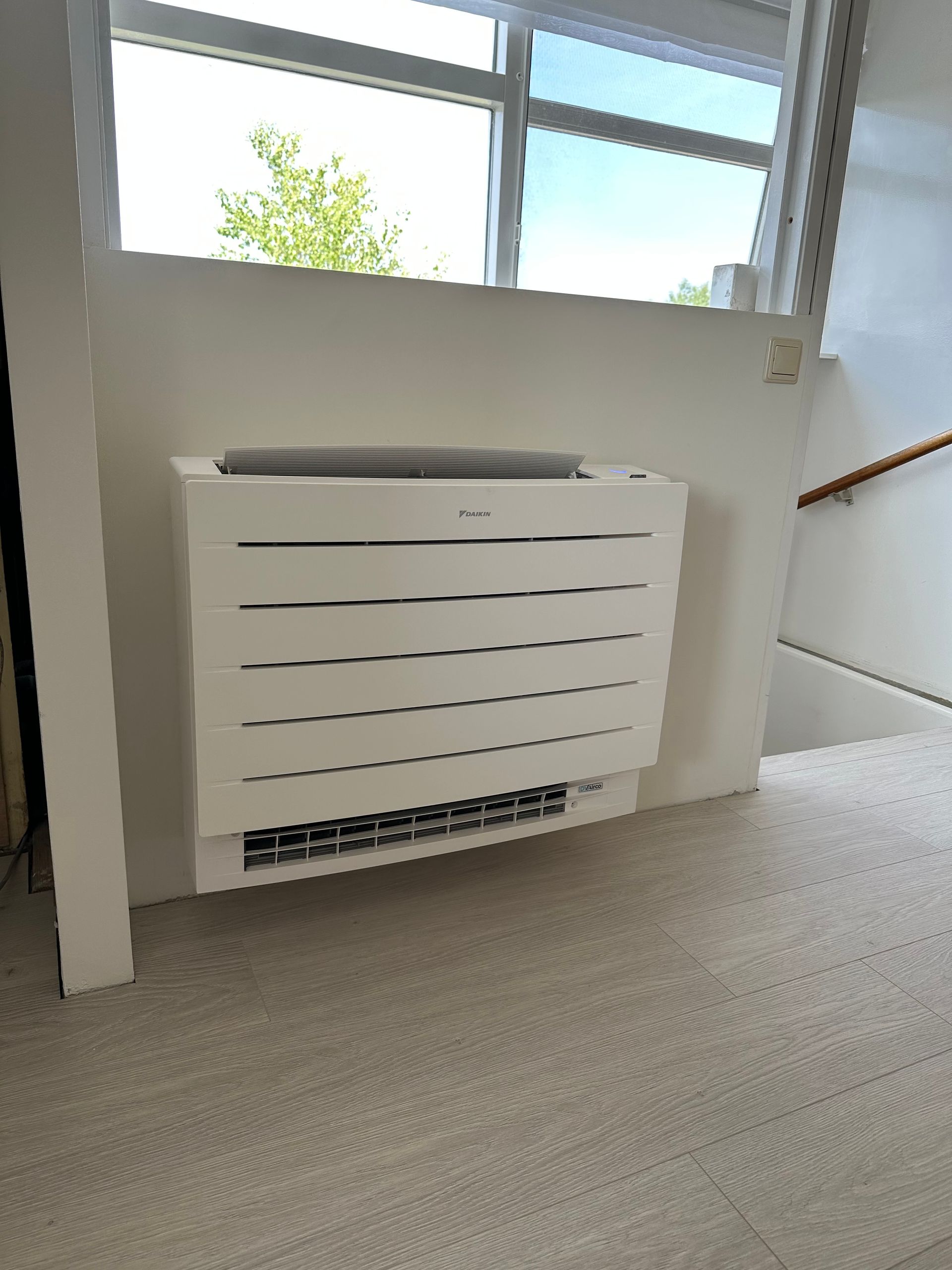Een witte airconditioner hangt aan de muur naast een raam.