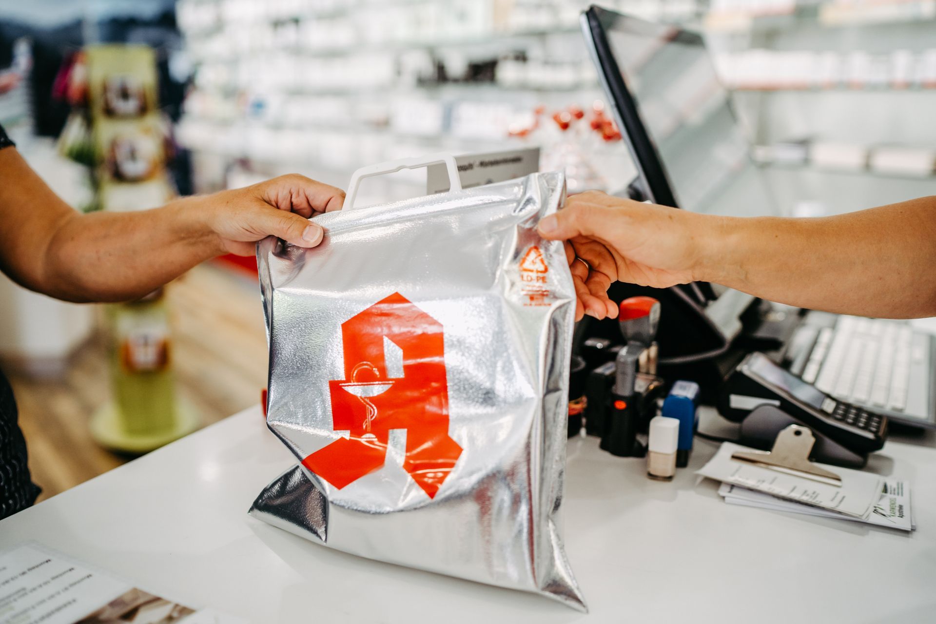 In einer Apotheke gibt eine Person einer anderen Person eine Tüte.