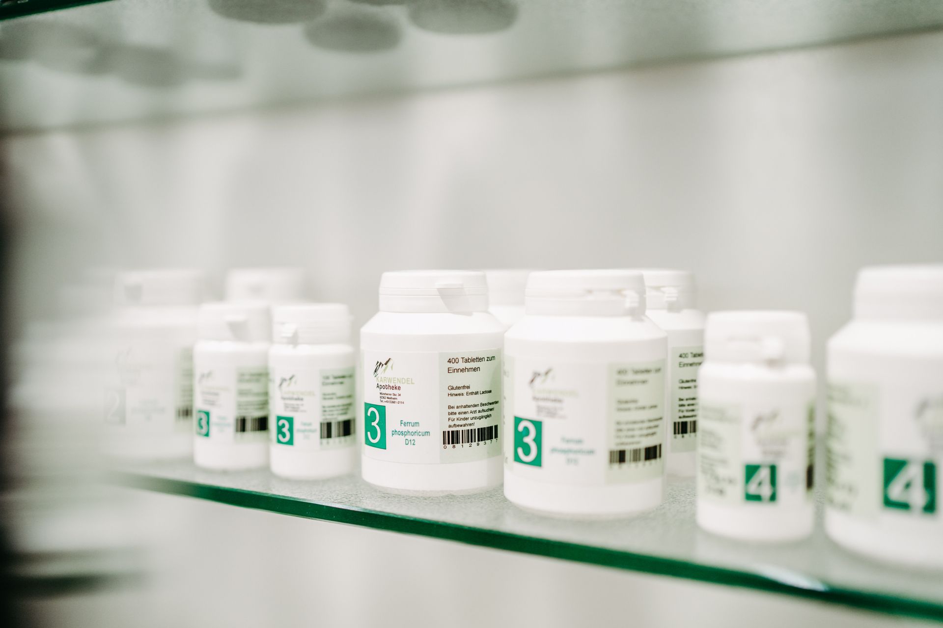 Eine Reihe weißer Flaschen auf einem Glasregal in einer Apotheke.