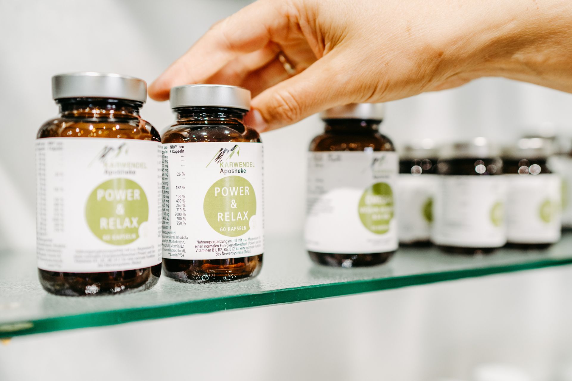 Eine Person greift nach einer Flasche Tabletten auf einem Glasregal.