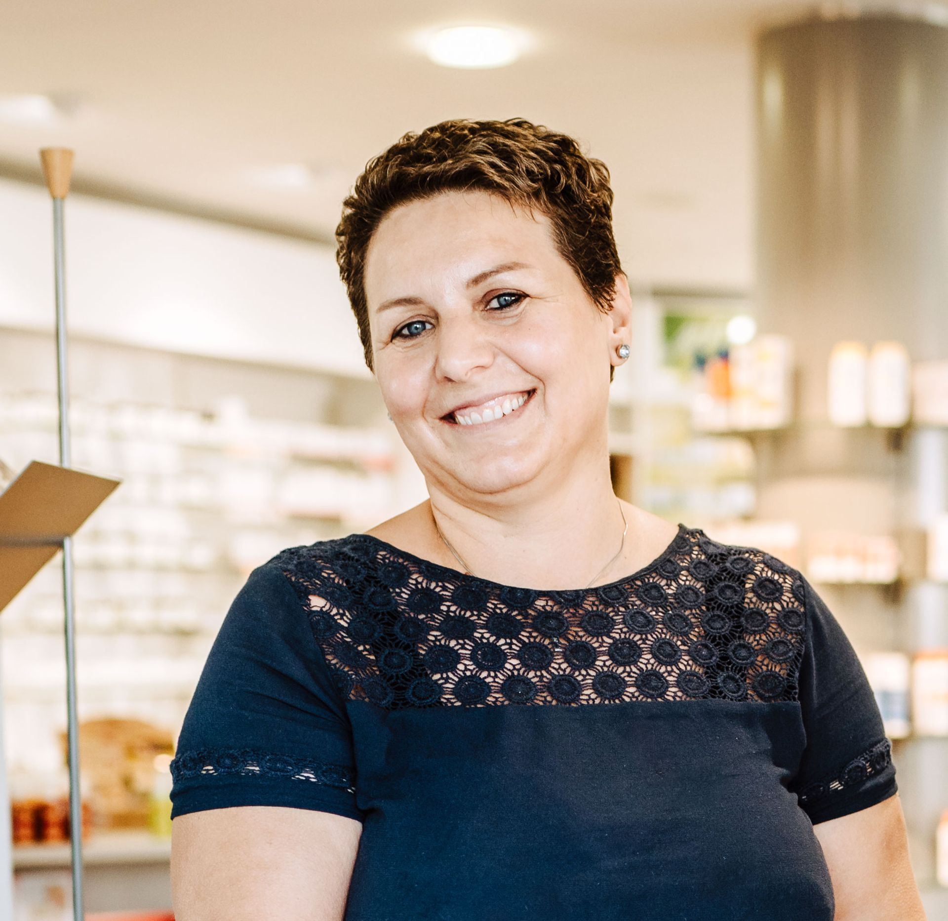 Eine Frau in einem blauen Spitzentop lächelt in die Kamera