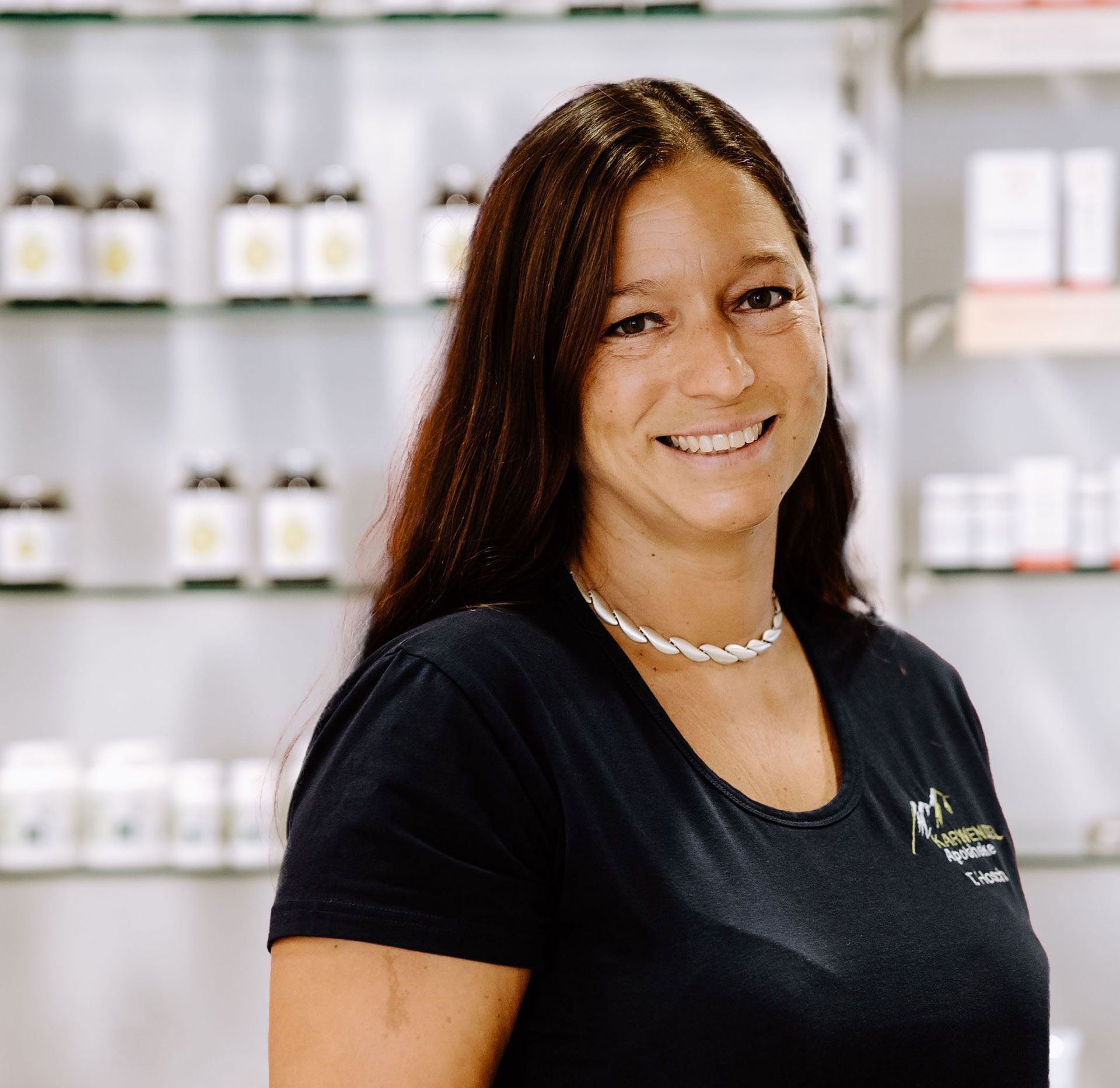 Eine Frau in einem schwarzen Hemd lächelt vor einem Regal mit Flaschen.