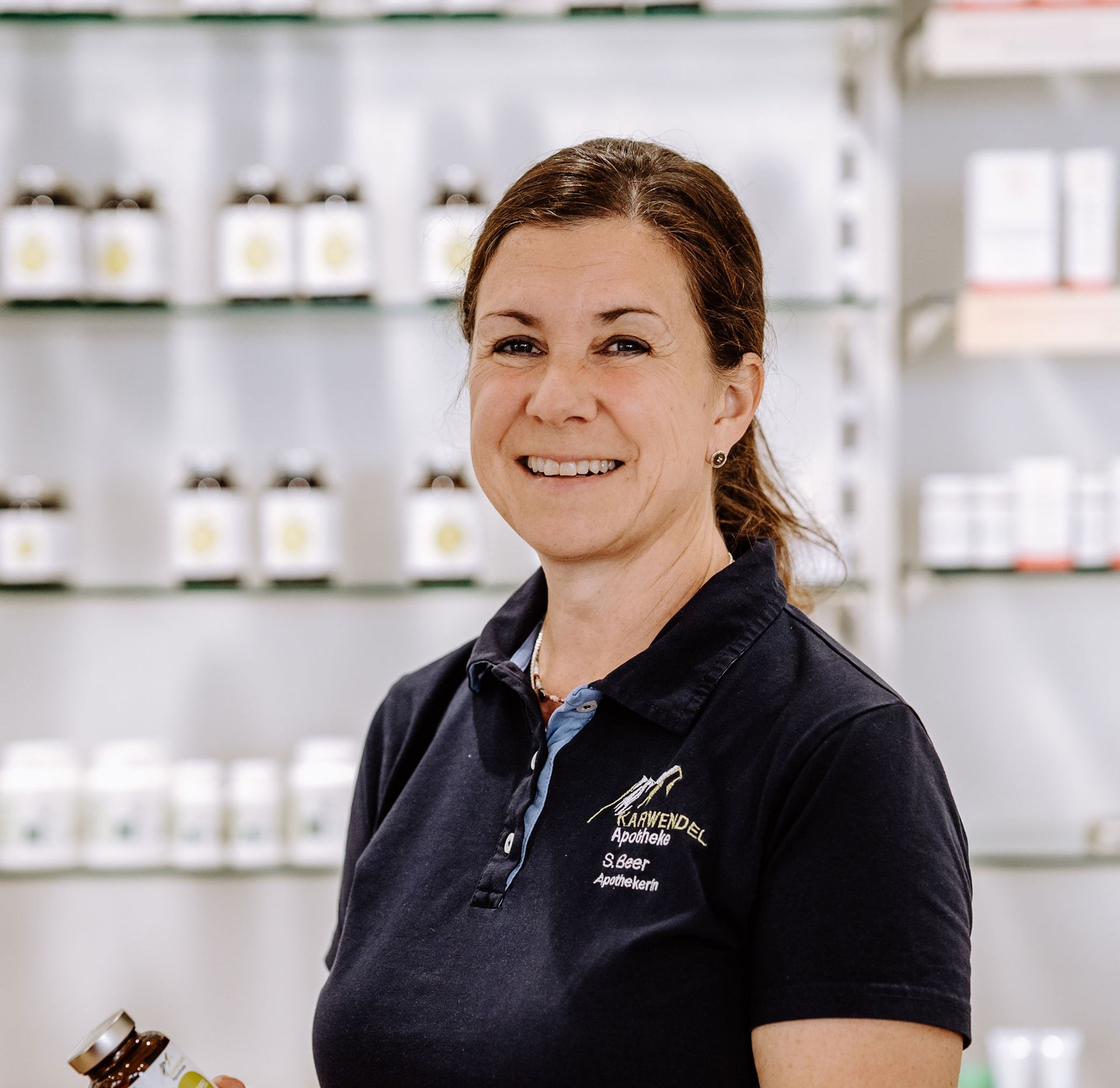Eine Frau in einem blauen Hemd lächelt und hält eine Flasche