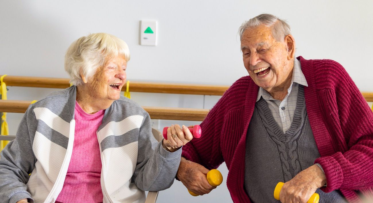 A man and a woman are laughing while holding dumbbells.