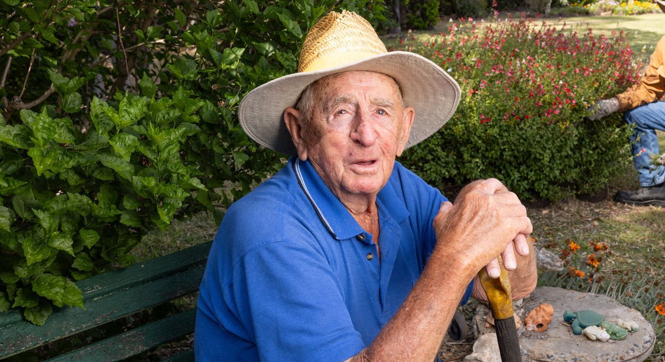 An elderly man wearing a straw hat and a blue shirt is sitting on a bench.