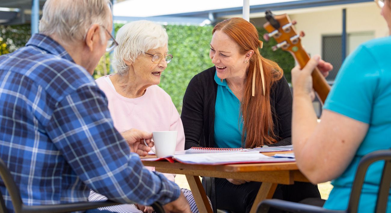 A group of elderly people are sitting at a table with a woman playing an ukulele.