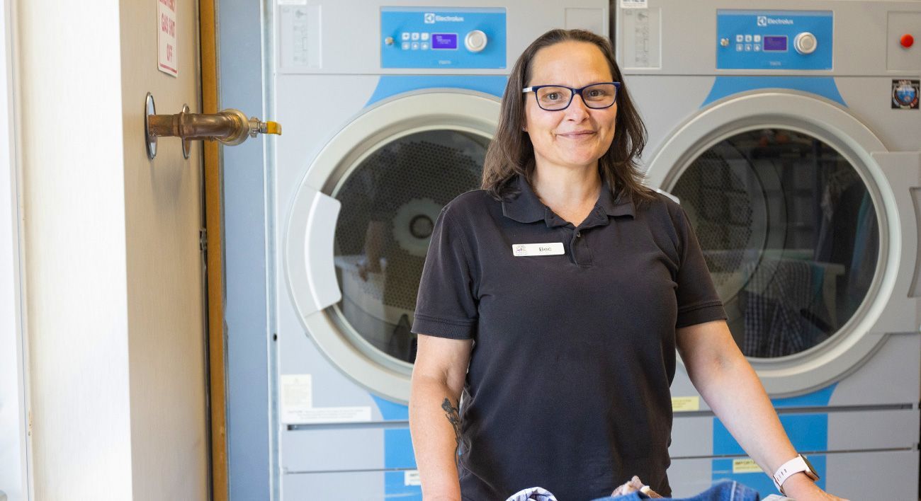 A woman is standing in front of a washing machine in a laundromat.