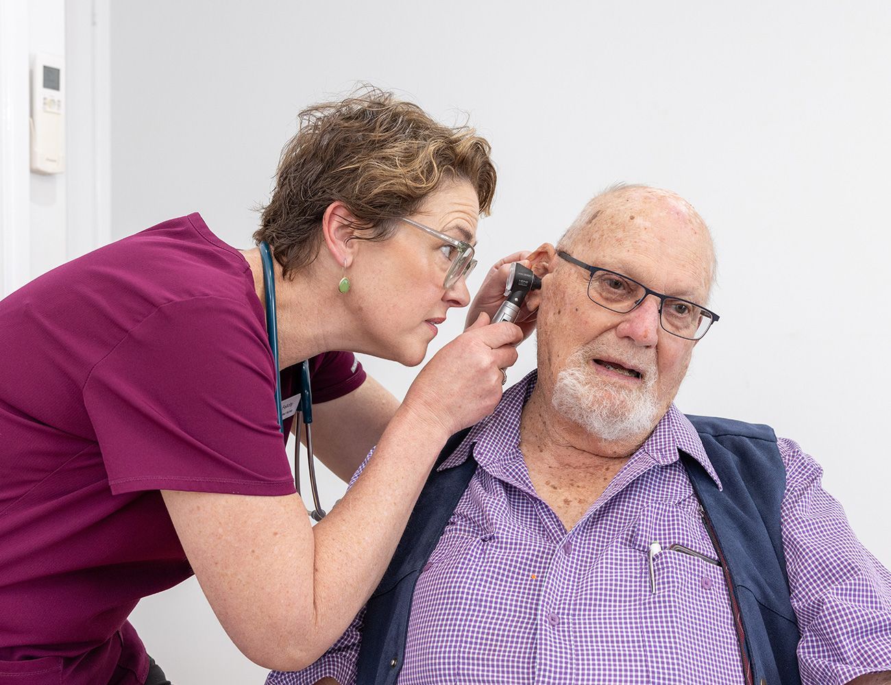 A nurse is examining an older man 's ear with a stethoscope.