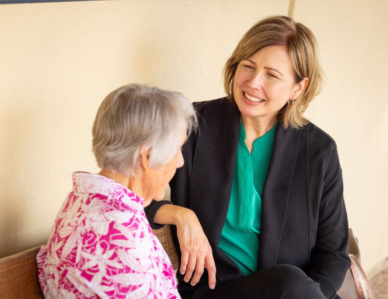 Two women are sitting on a bench talking to each other.