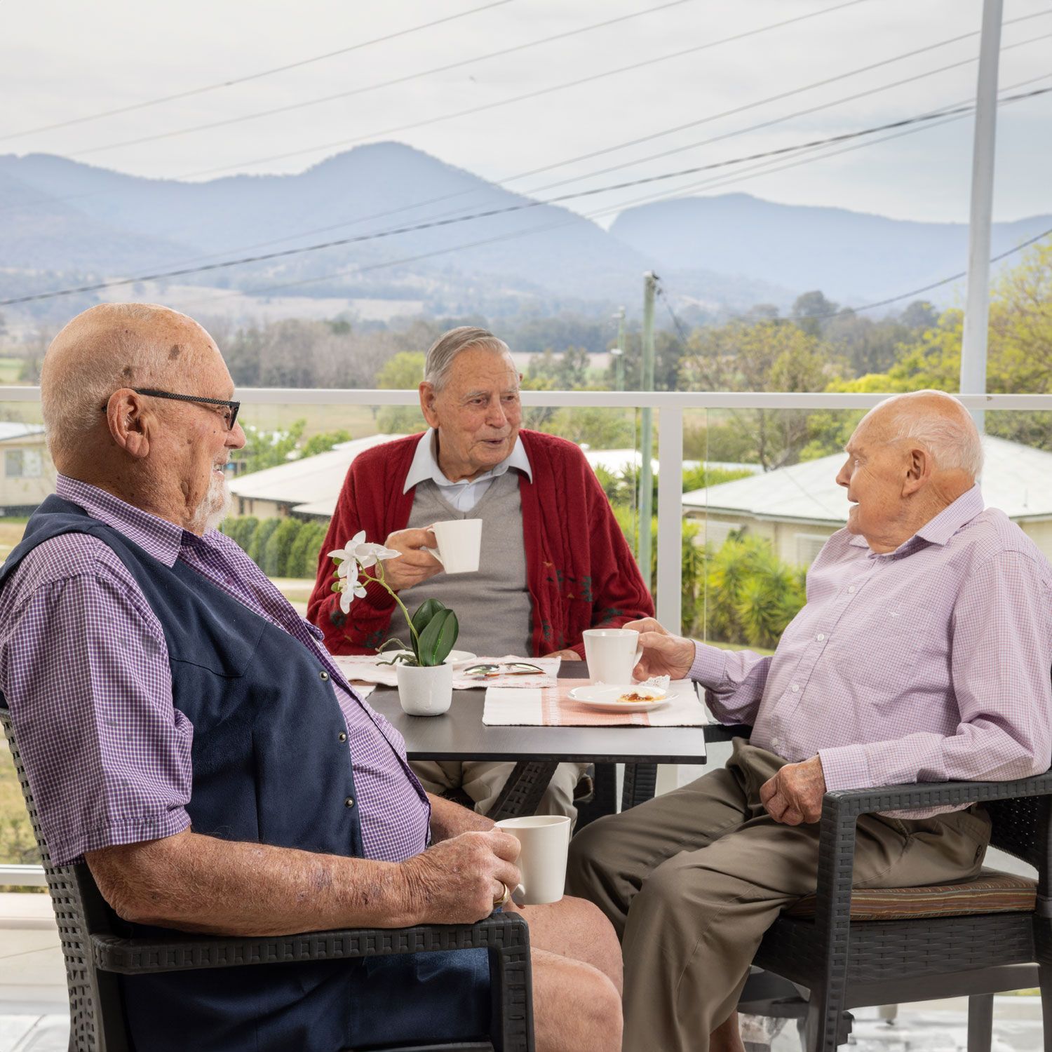 Three older men are sitting at a table drinking coffee.