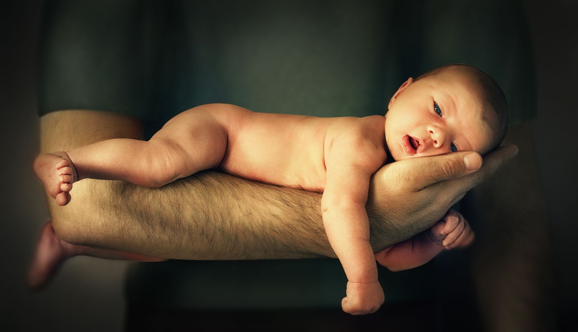 Een pasgeboren kind ligt op z'n buik op de arm van een man.