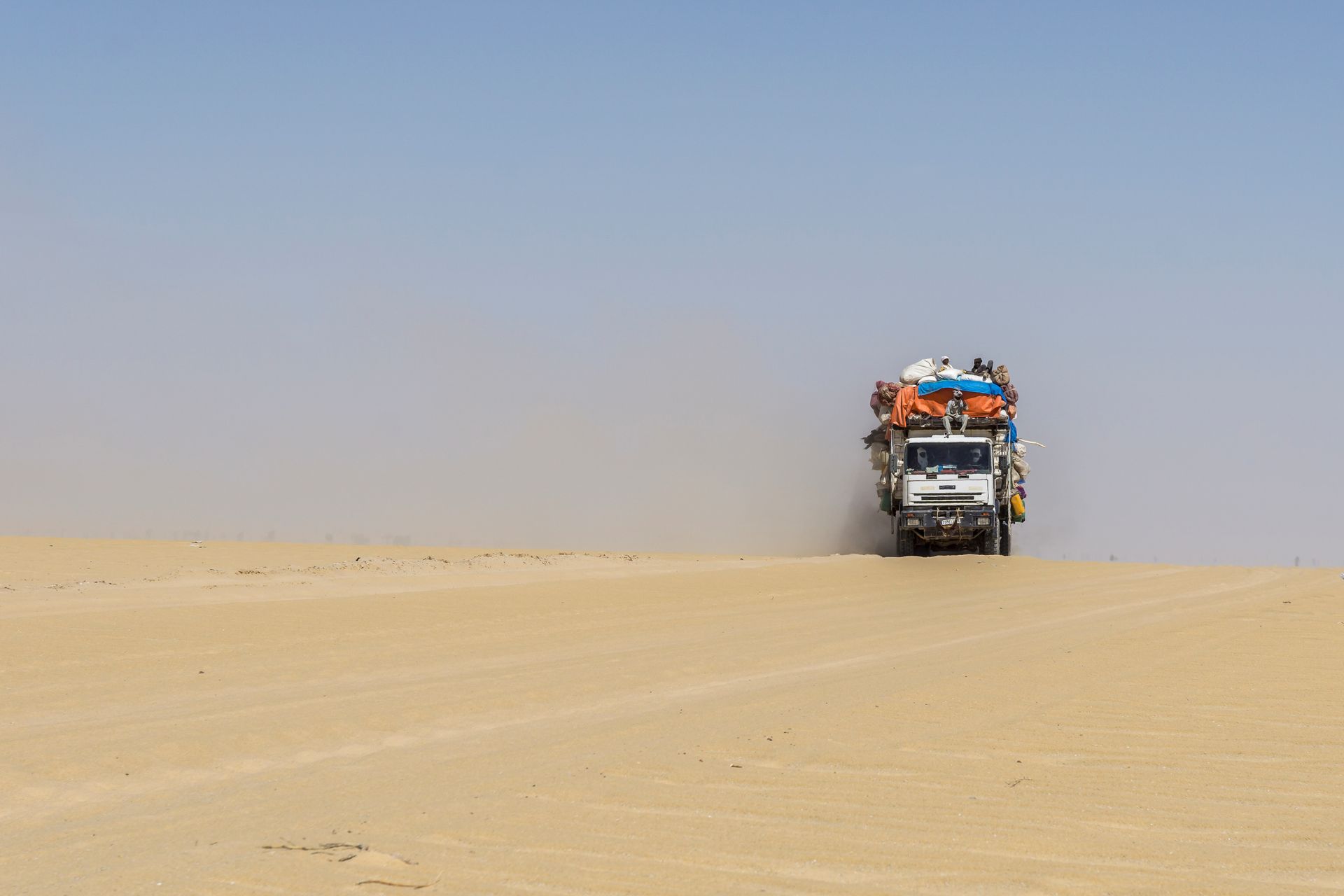 Een vrachtwagen met goederen en mensen rijdt door de woestijn.