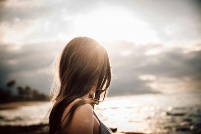 A woman is standing on the beach looking at the ocean.