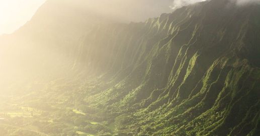 An aerial view of a mountain covered in trees with the sun shining through the clouds.