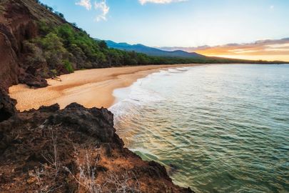 A beach with mountains in the background and a body of water in the foreground.