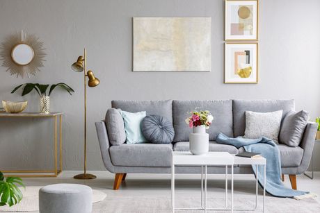 Modern Nordic Scandinavian styled apartment, large sofa with blank wall behind. Interior with many details, coffee table, plant, books, pastel colors. Copy space mock up for designers