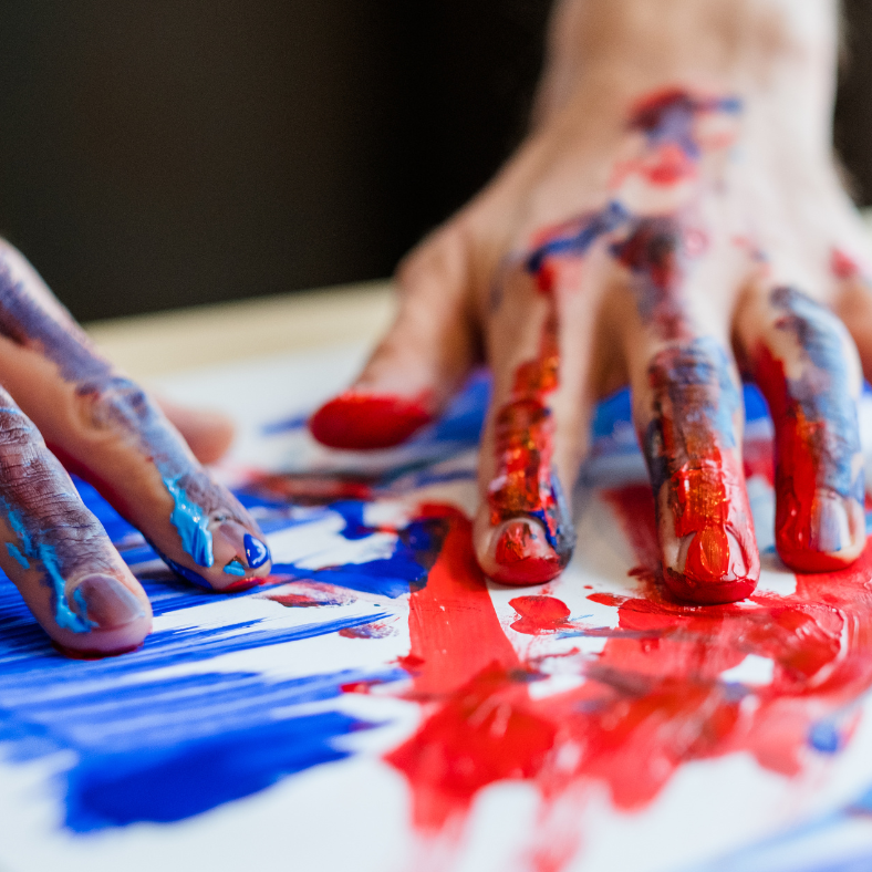 hands finger painting with red and blue paint.