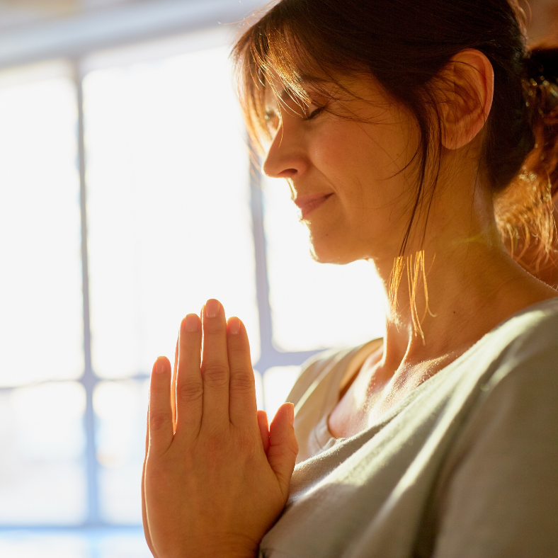 A woman is praying with her eyes closed and her hands folded in prayer.
