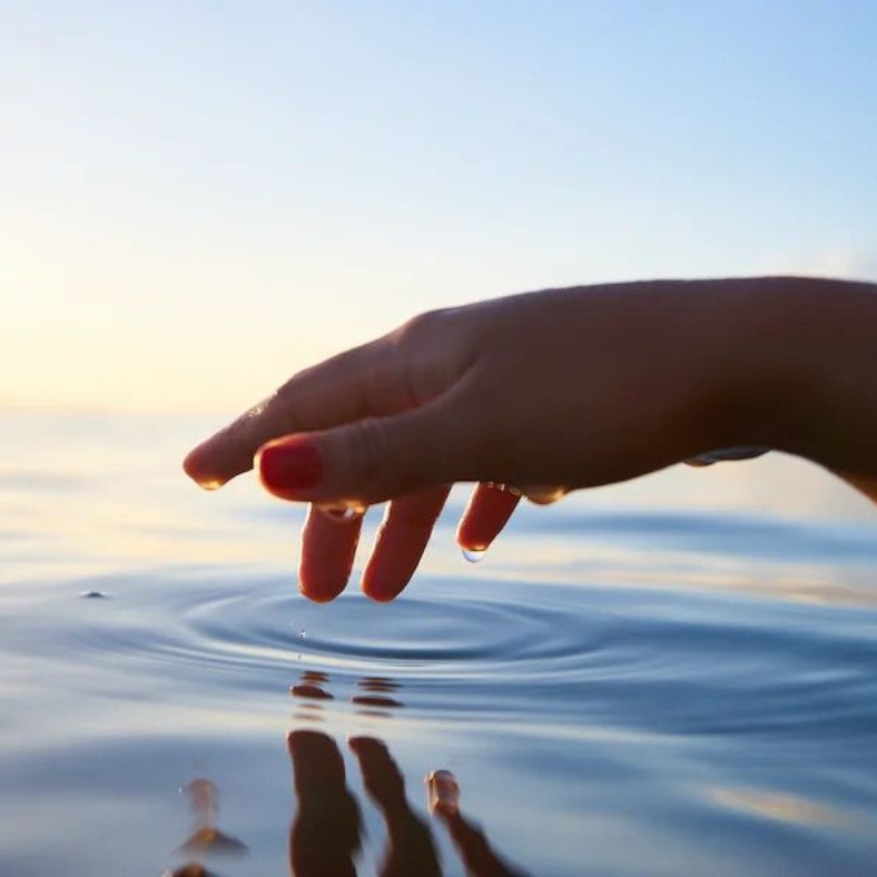 A woman 's hand is touching the surface of a body of water