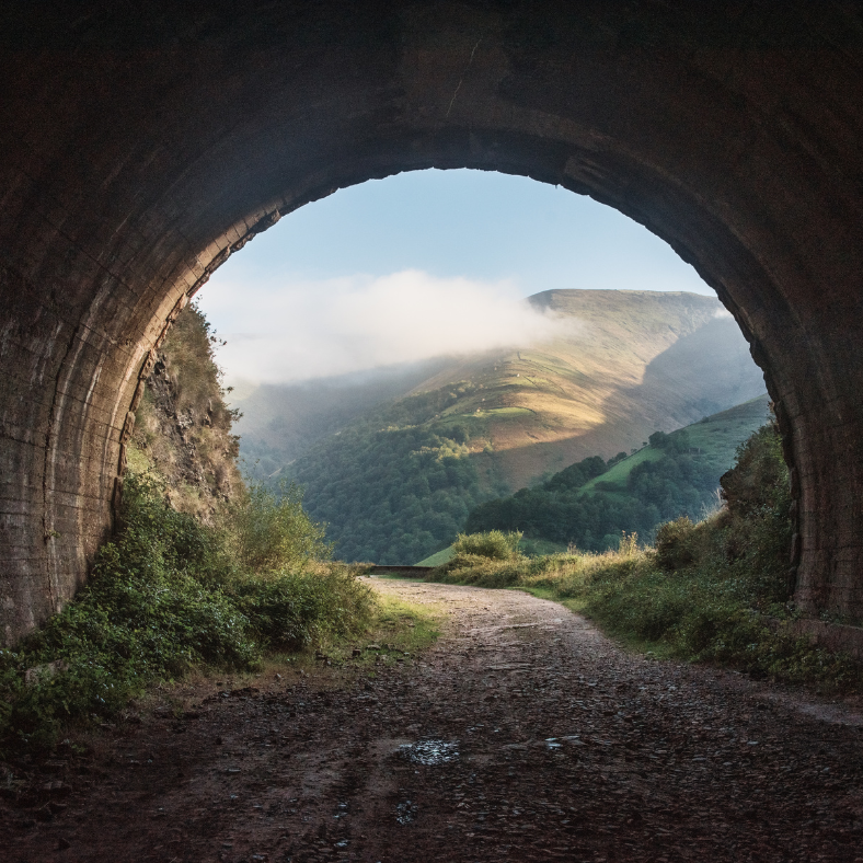A tunnel leading to a valley with mountains in the background