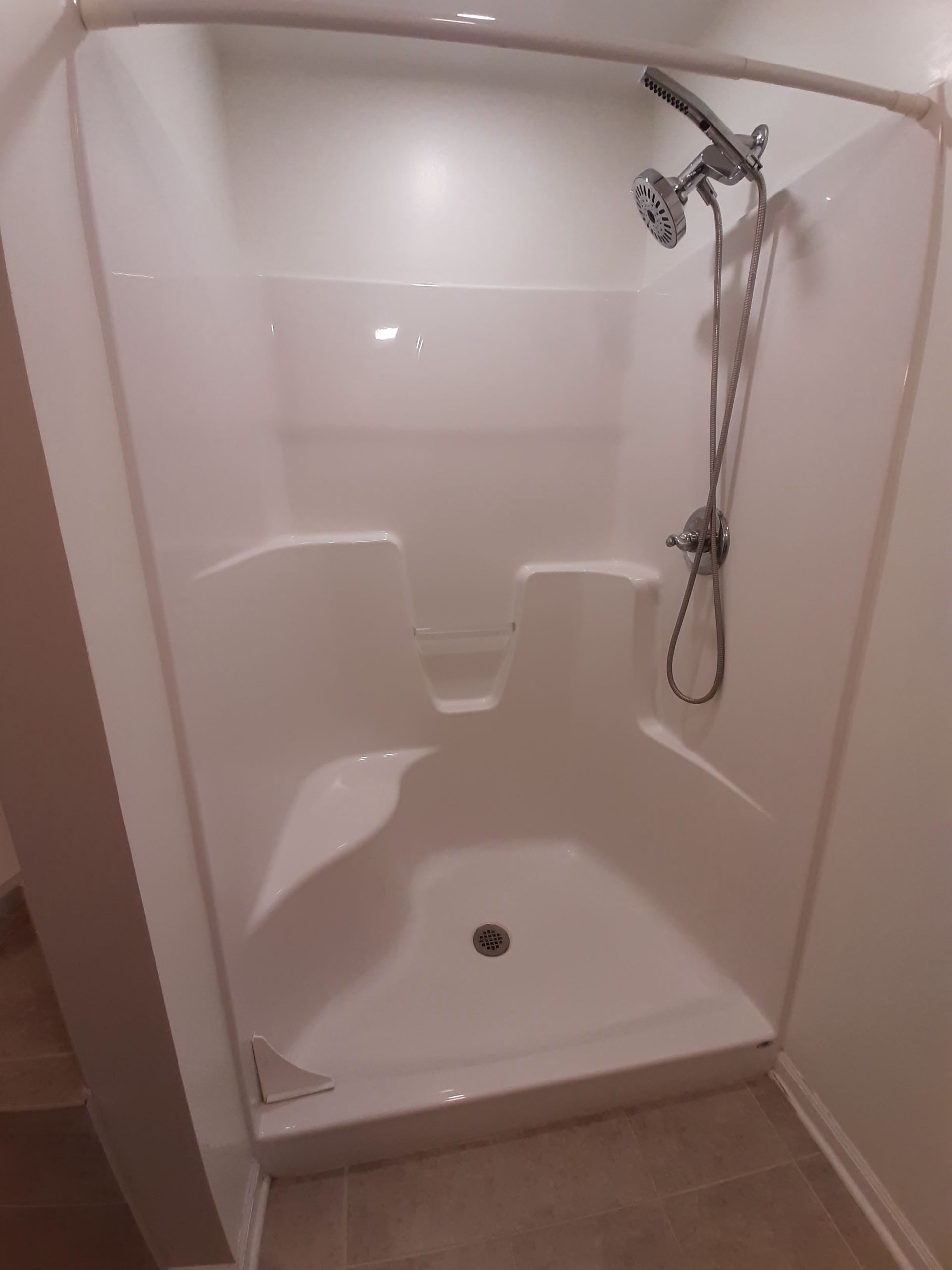 A white shower stall with a shower head in a bathroom.