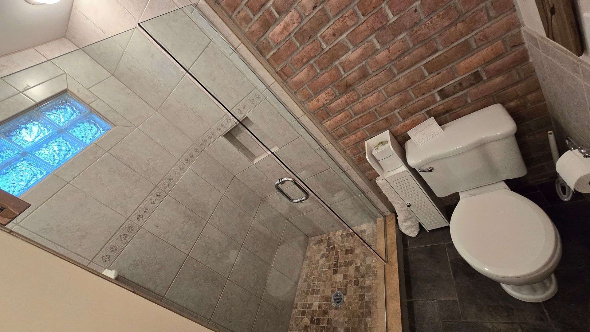 A bathroom with a toilet , shower and brick wall.
