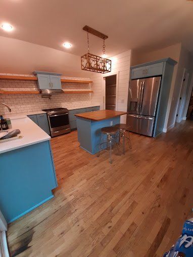 A kitchen with blue cabinets , stainless steel appliances , hardwood floors and a large island.