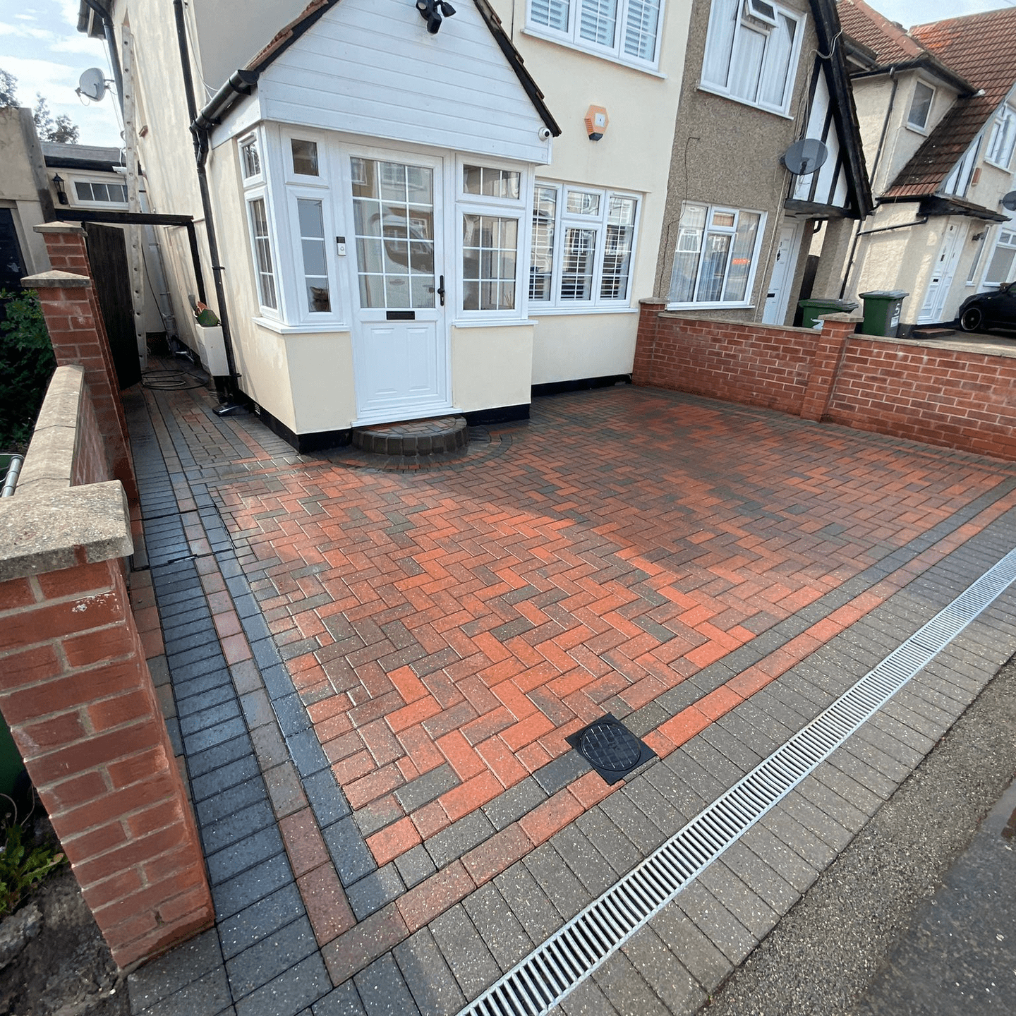 Brick driveway with red and grey paving, leading to a white front door.