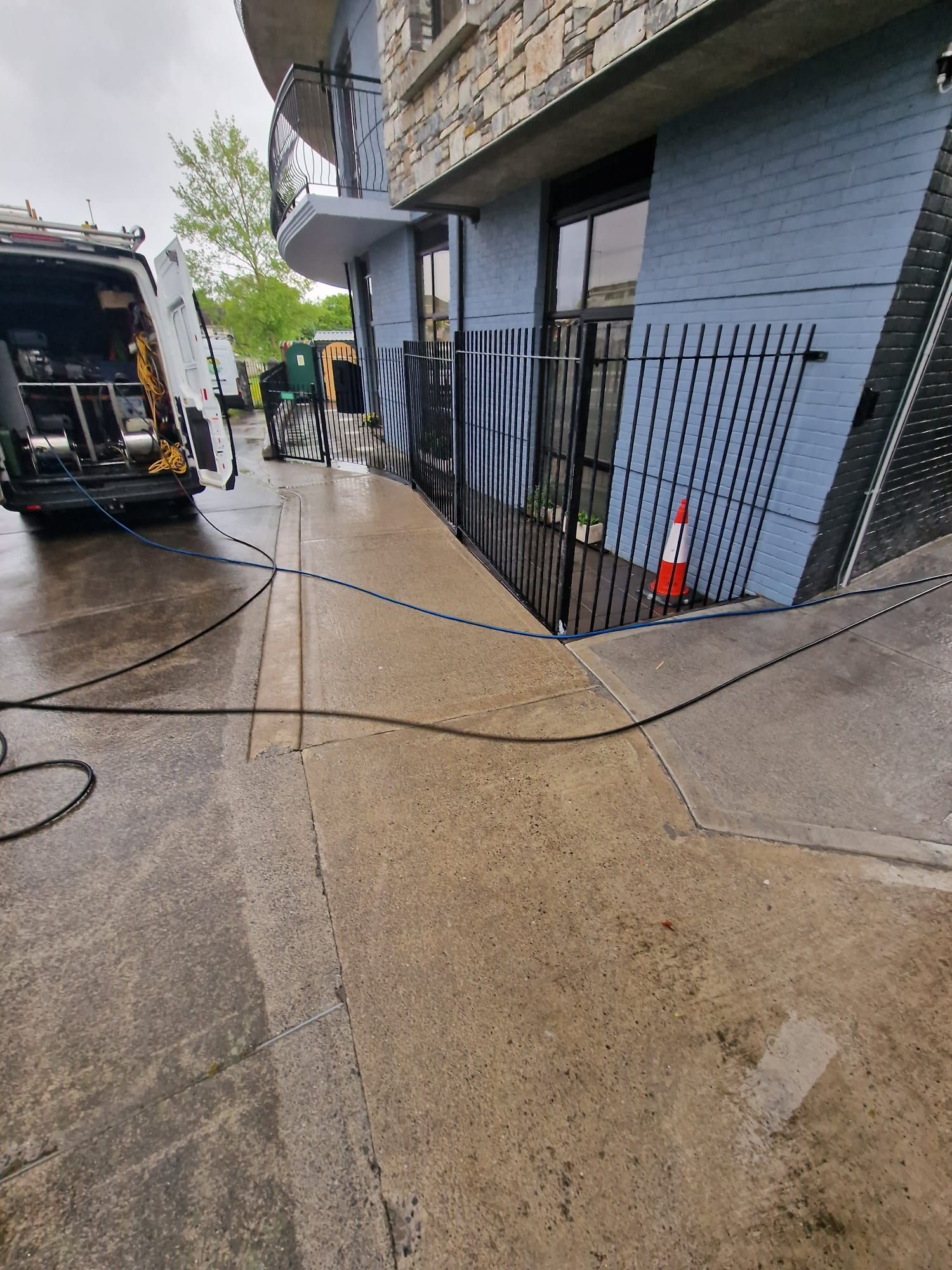 Exterior view of a building with a worker and a van, power washing the concrete walkway.