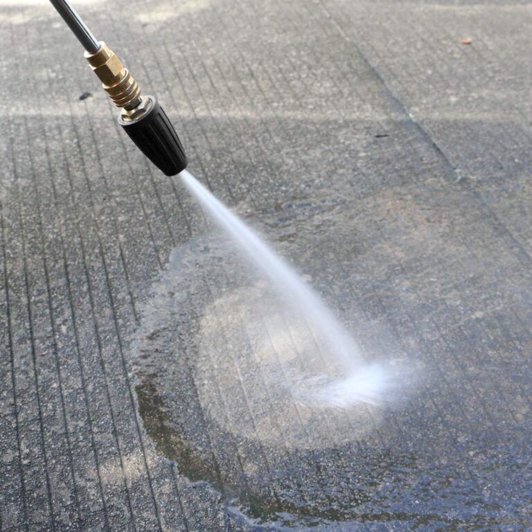 Pressure washer spraying water on a concrete surface, cleaning a circular area.