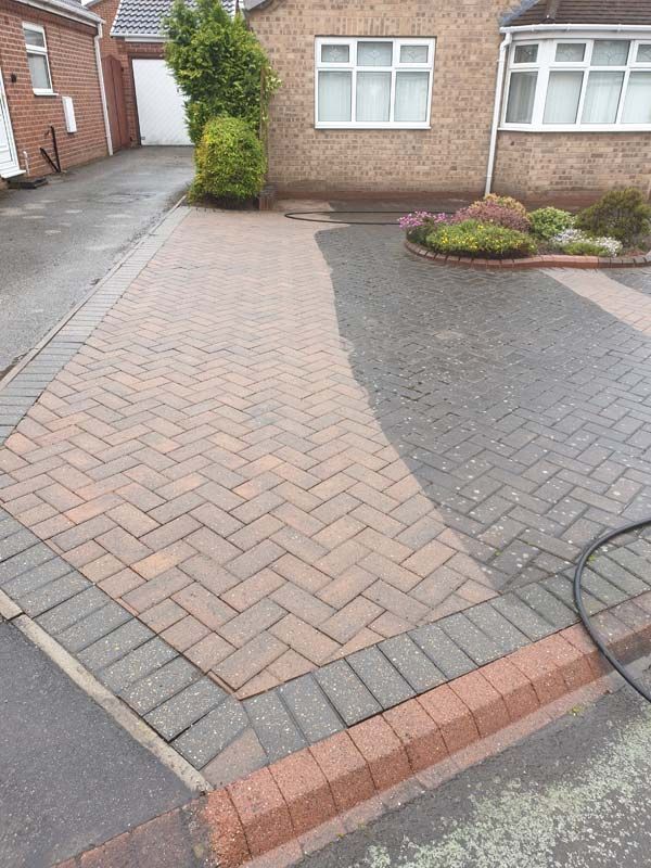 Driveway partially cleaned, showing red brick pavers and gray border, house in background.