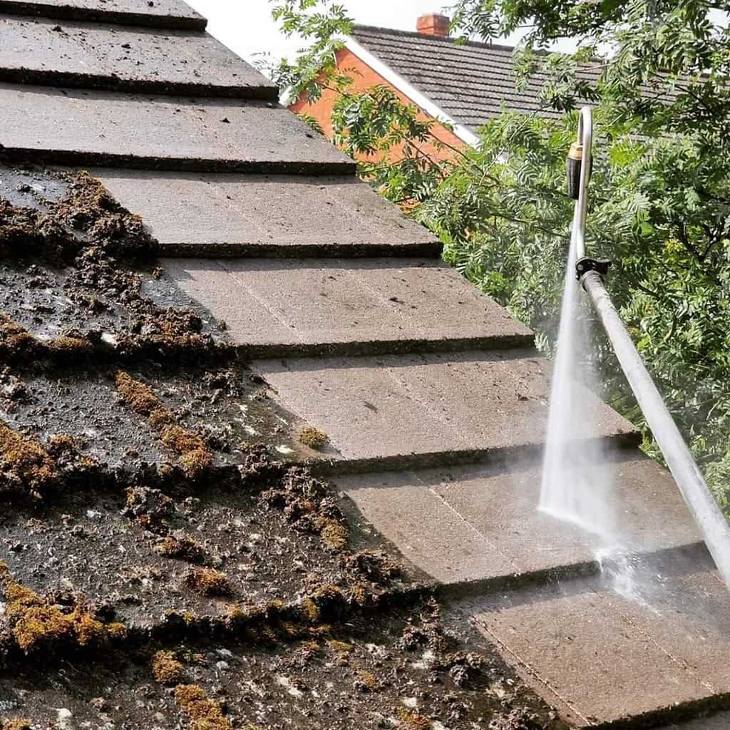 Roof tiles being cleaned with a pressure washer; dirty moss on left side, clean on the right.