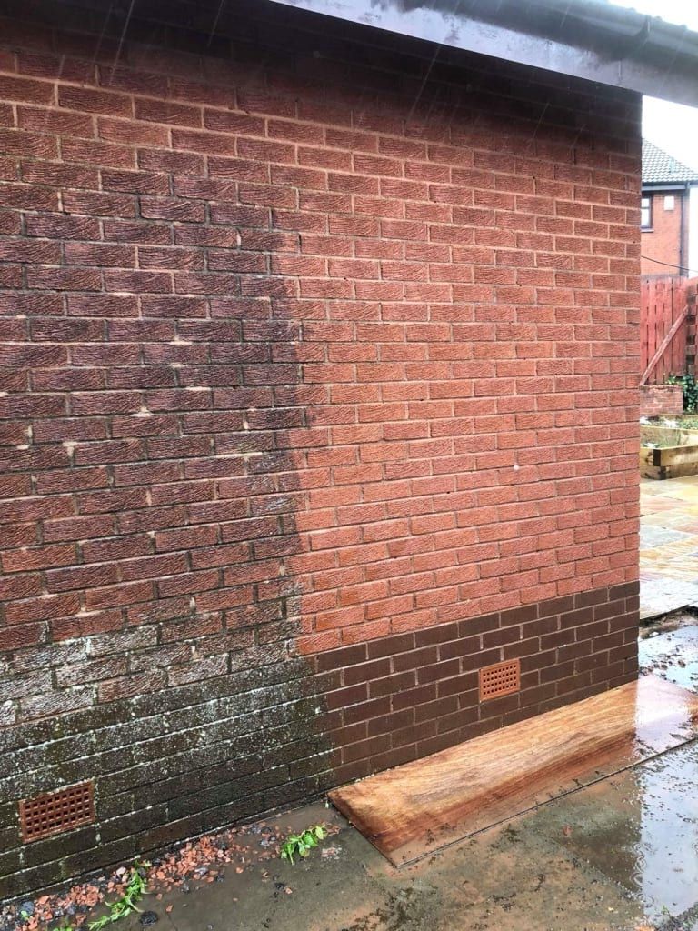 Brick wall, partially cleaned with a pressure washer. Dark, dirty side contrasts with the clean, red bricks.