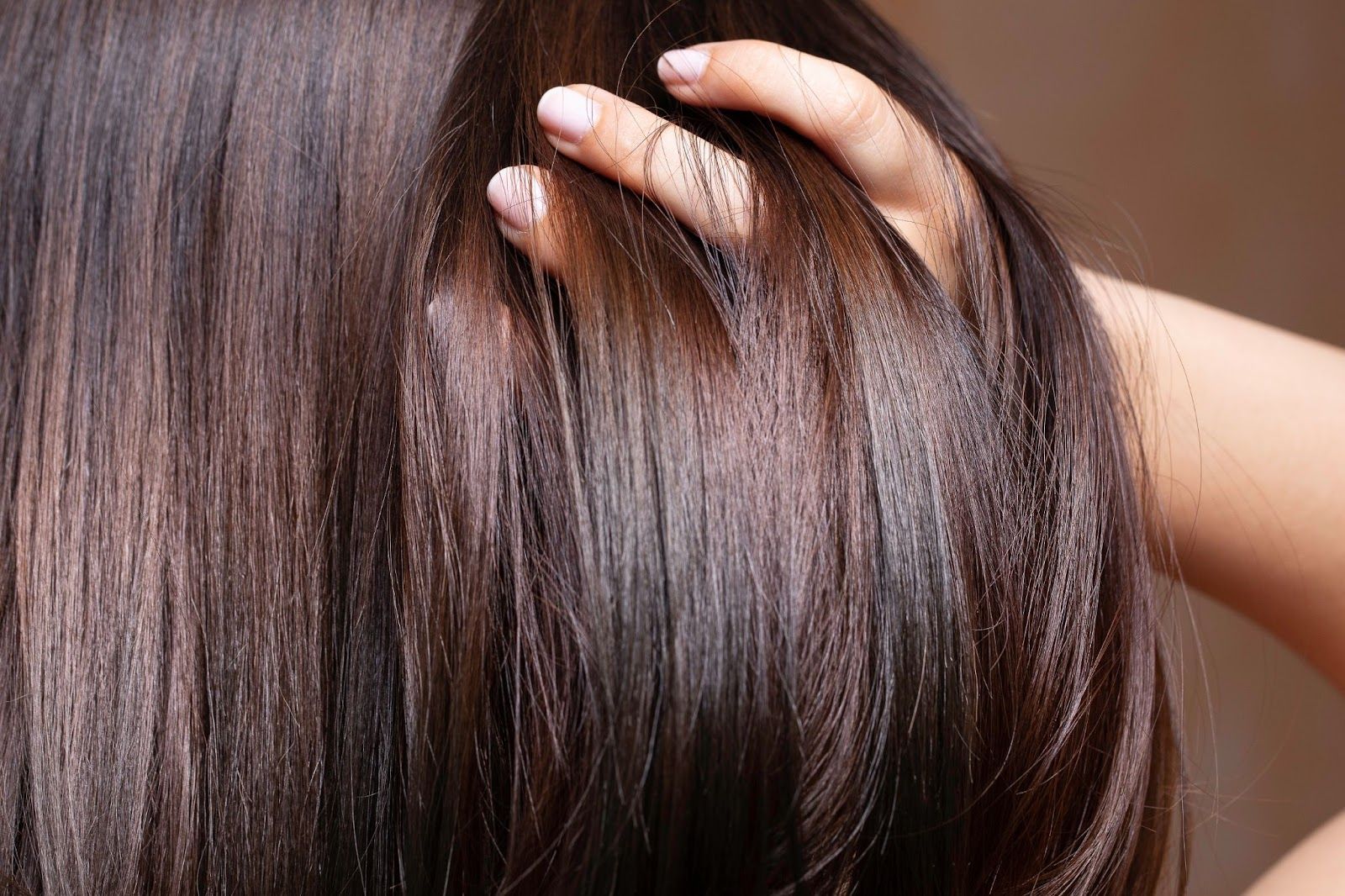 A woman with long brown hair is using a comb to style her hair, looking relaxed and attentive.