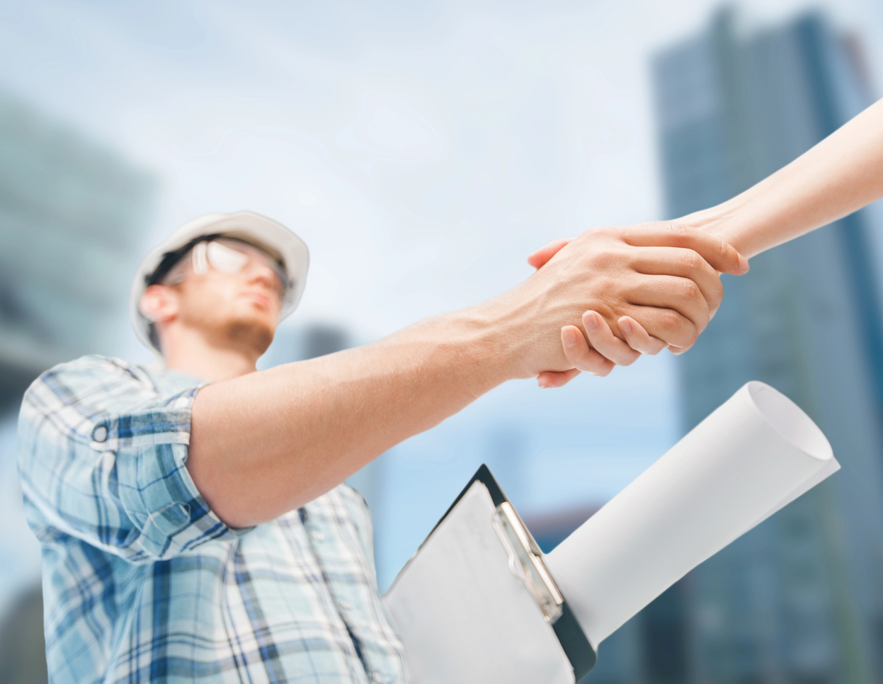 Trabajador de la construcción estrechando manos frente a los rascacielos, sosteniendo planos.