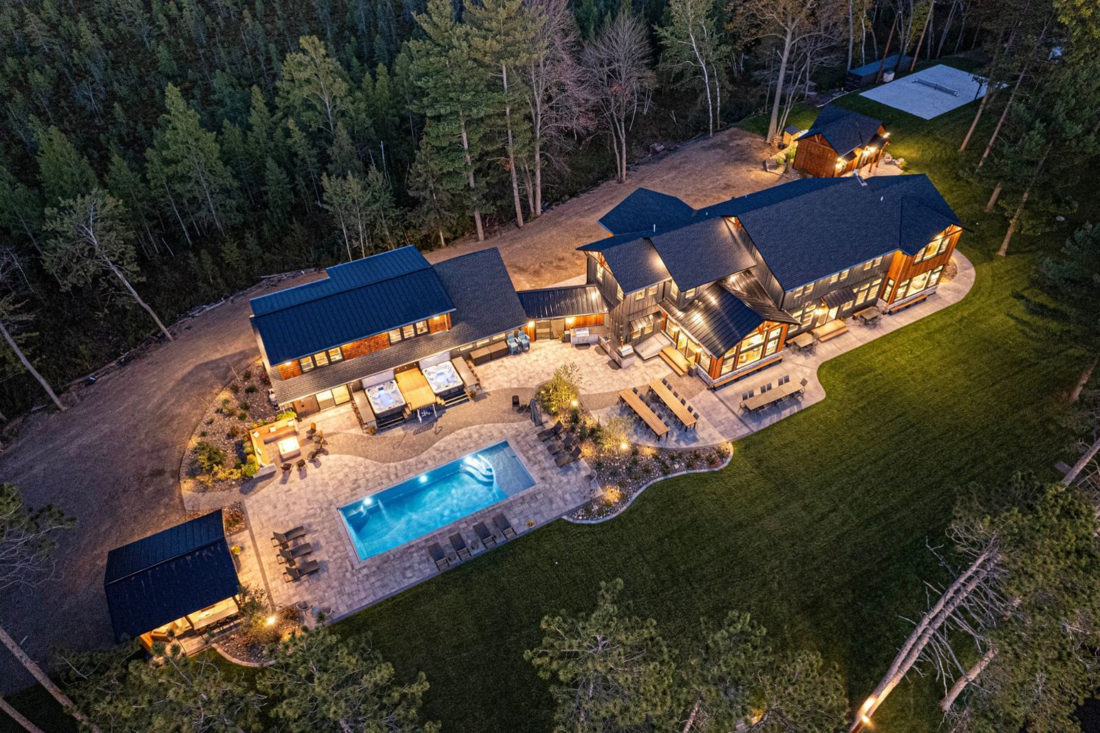 Aerial view of a large house with a pool and multiple outbuildings, set in a forest.