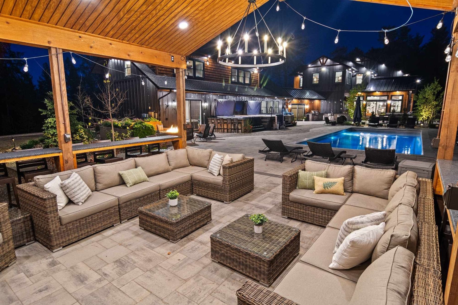 Outdoor patio with wicker sectional sofas and pool, lit with string lights and a chandelier at night.