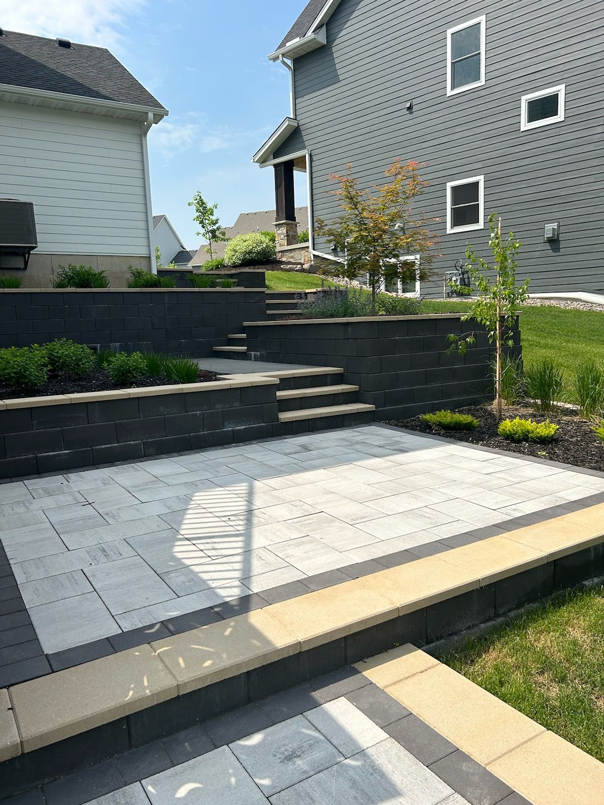 Patio with gray pavers, retaining walls with steps, and two-story houses.
