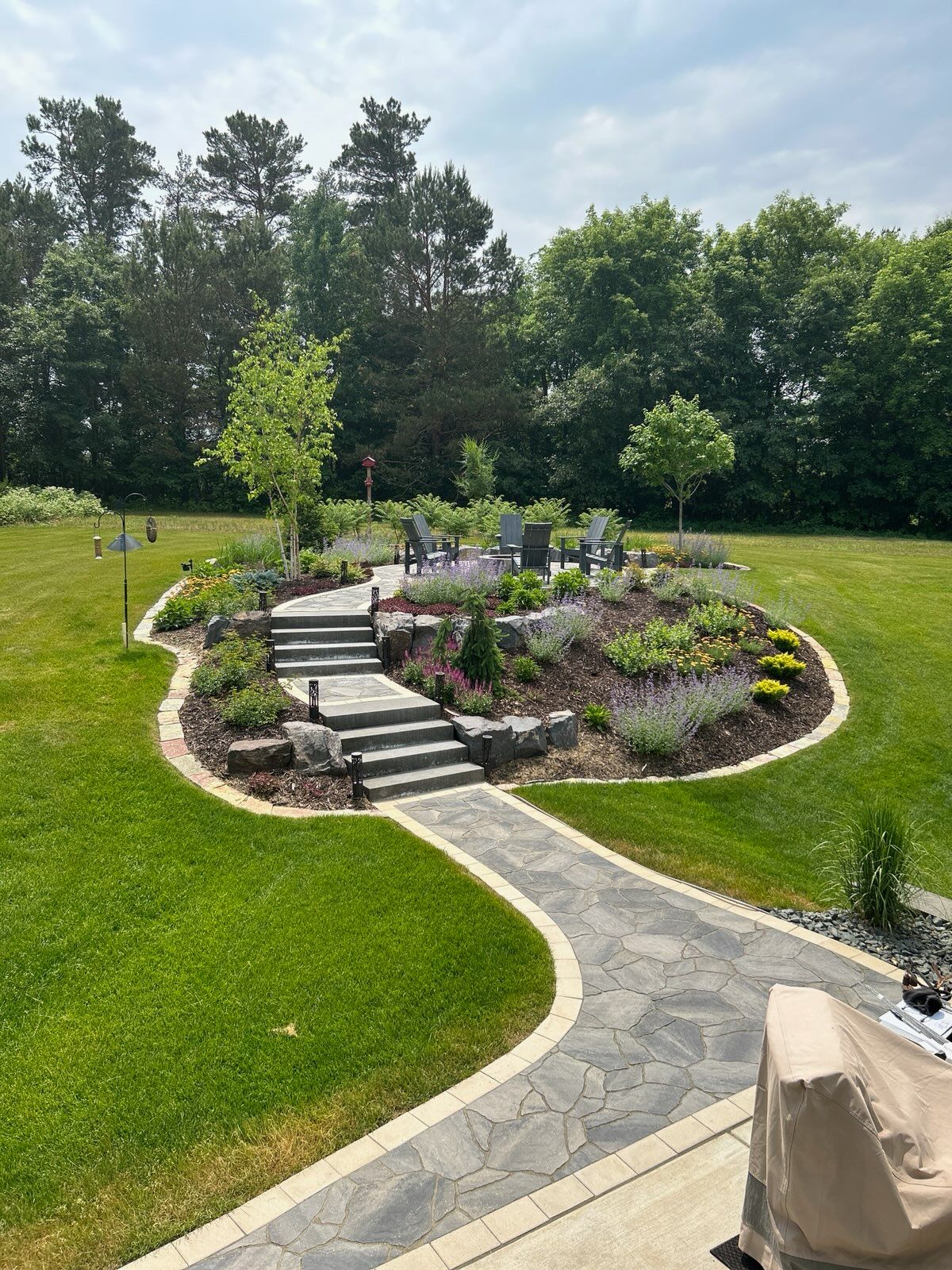 Stone path leads to tiered garden patio with seating, surrounded by landscaping and lawn.