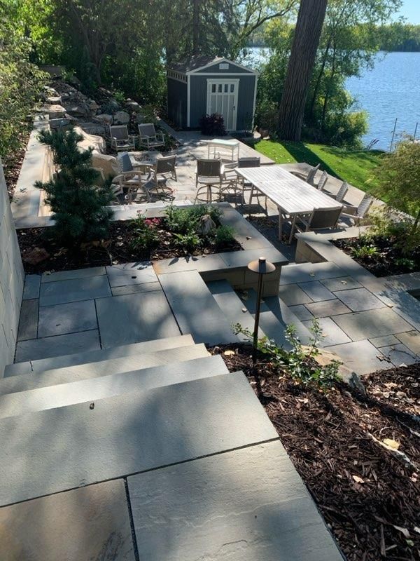 Stone patio and steps leading to a lakefront gathering space with dining and lounge seating.