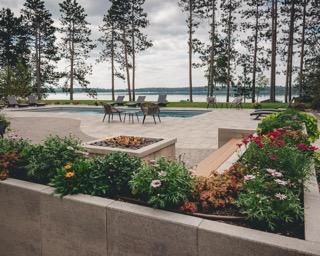 Stone patio with pool, fire pit, lake, and colorful landscaping.