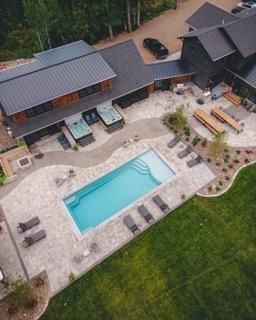 Aerial view of a modern home with a pool, hot tubs, and outdoor seating on a green lawn.