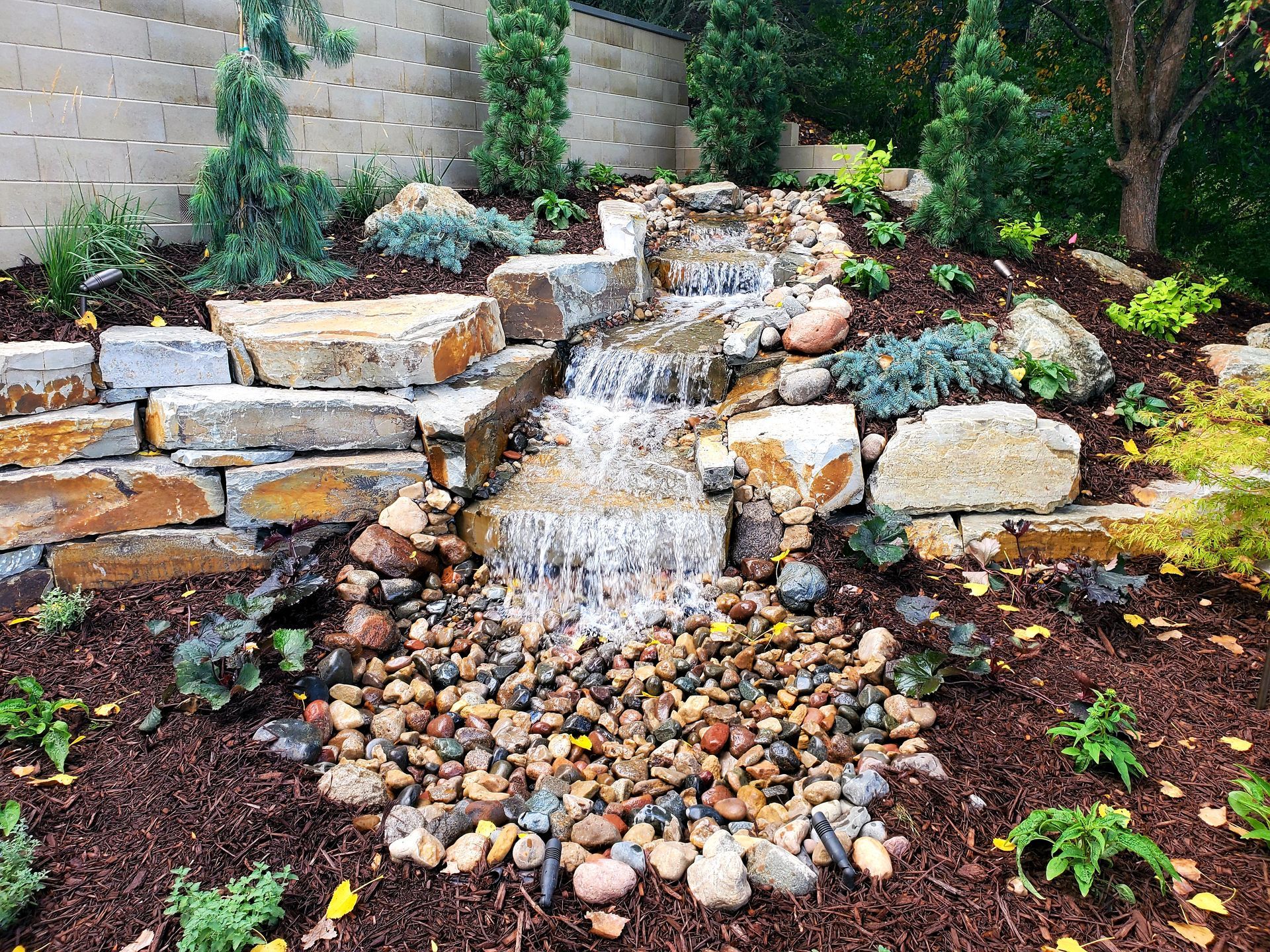 Water cascading down a stone waterfall feature in a landscaped garden bed.