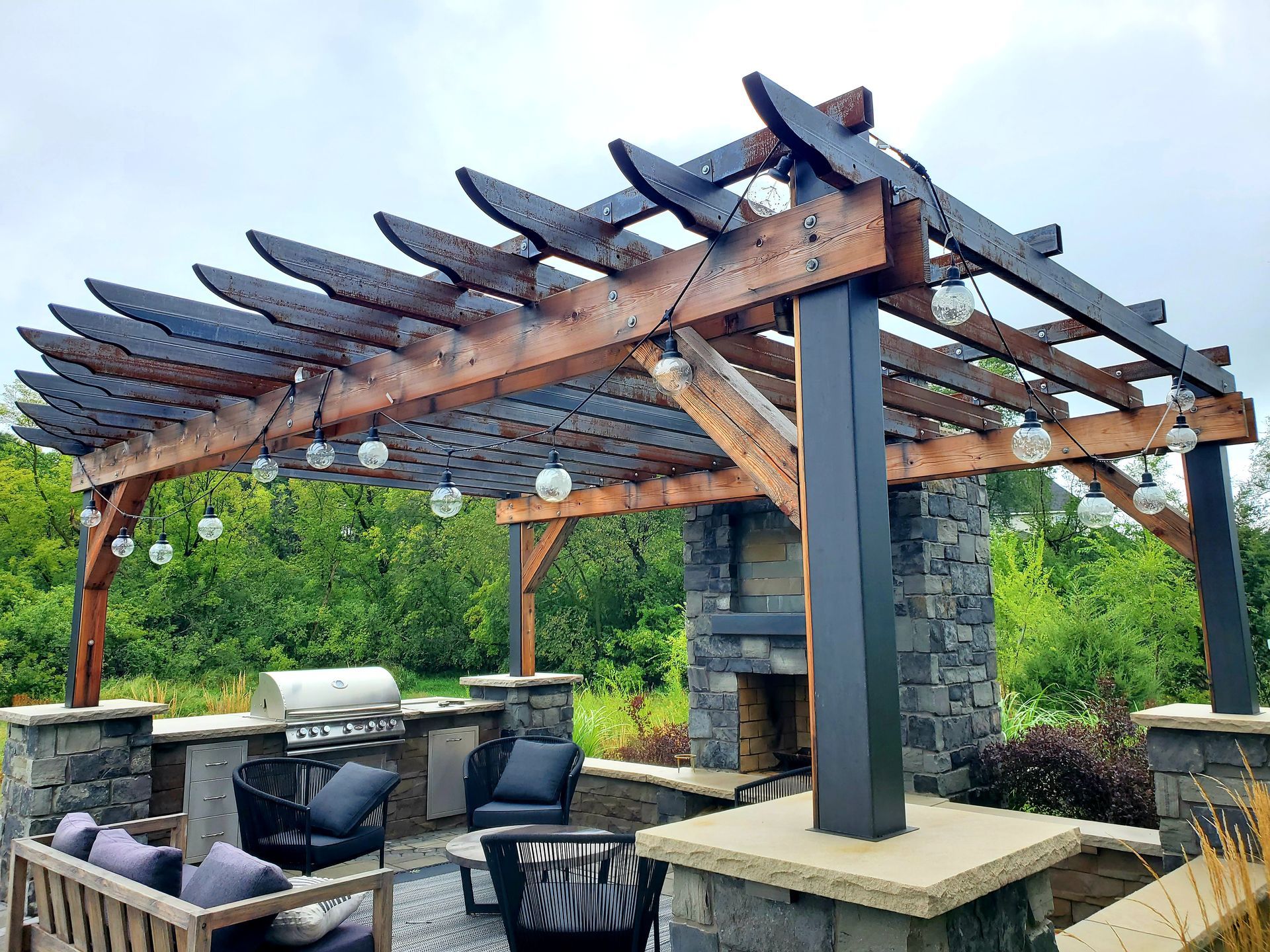 Outdoor kitchen and seating area with wooden pergola and fireplace.